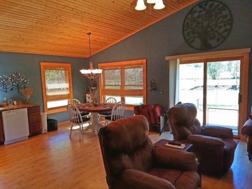 Cozy living space with wooden ceiling, dining area, and large windows overlooking a green landscape.