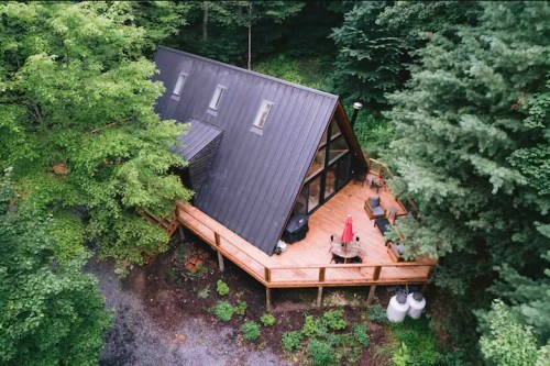 Aerial view of a modern A-frame cabin surrounded by lush greenery and a wooden deck.