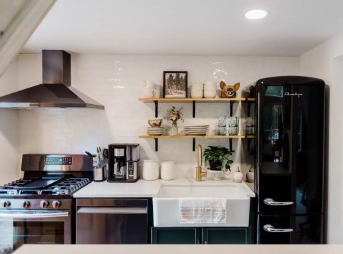 Modern kitchen featuring a black fridge, stainless steel appliances, open shelves with decor, and a farmhouse sink.