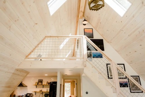 Interior of a modern A-frame house with wooden walls, a staircase, and large windows letting in natural light.