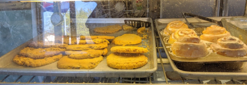 A display case with freshly baked cookies and cinnamon rolls on metal trays.