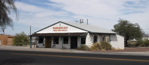 A small, white building with a sloped roof and a sign reading "Roadrunner Java" on a sunny day.