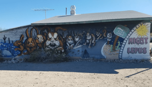 Mural on a building depicting large, cartoonish rabbits with a "Night of the Lepus" movie theme. Desert landscape in foreground.