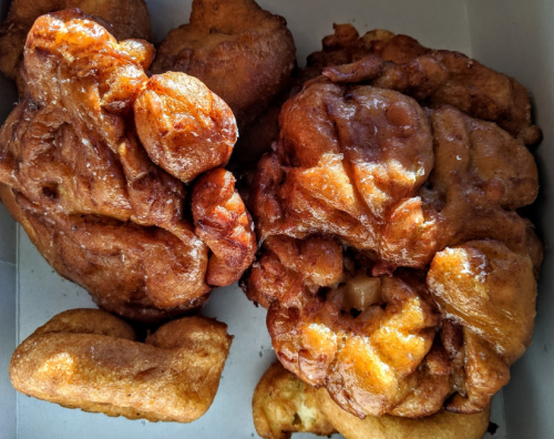 Two golden-brown fried pastries, one resembling a large doughnut and the other a smaller, elongated shape, in a box.