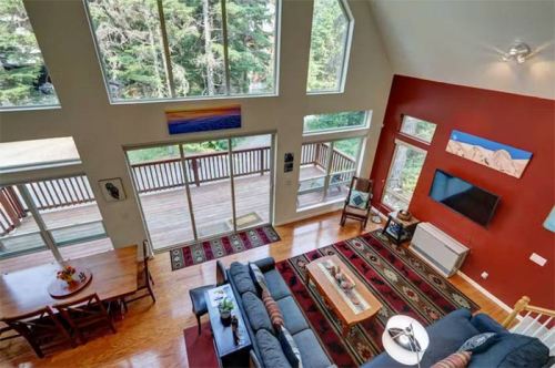 A spacious living area with large windows, a cozy sofa, and a dining table, surrounded by trees outside.