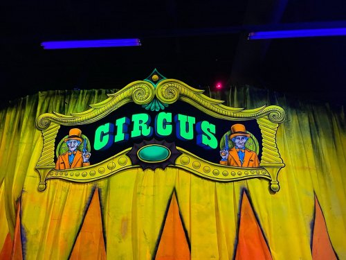 Colorful circus sign with the word "CIRCUS" and two characters in orange suits, set against a vibrant yellow backdrop.