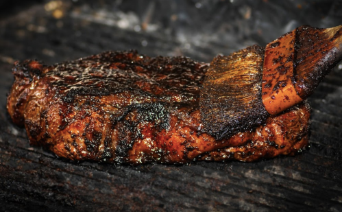 A juicy steak on a grill, being brushed with a flavorful marinade, showcasing a rich, charred exterior.