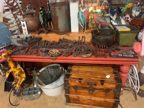 A cluttered display of vintage tools, metal objects, and decorative items on a red table in a rustic setting.