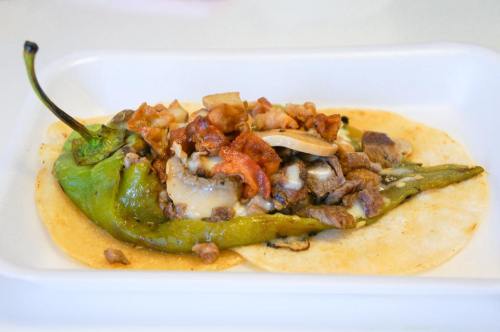 A green chili pepper stuffed with meat, cheese, and toppings, served on two corn tortillas.