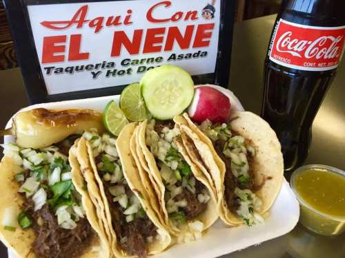 A plate of tacos filled with carne asada, topped with onions and cilantro, served with lime, radish, and a soda.
