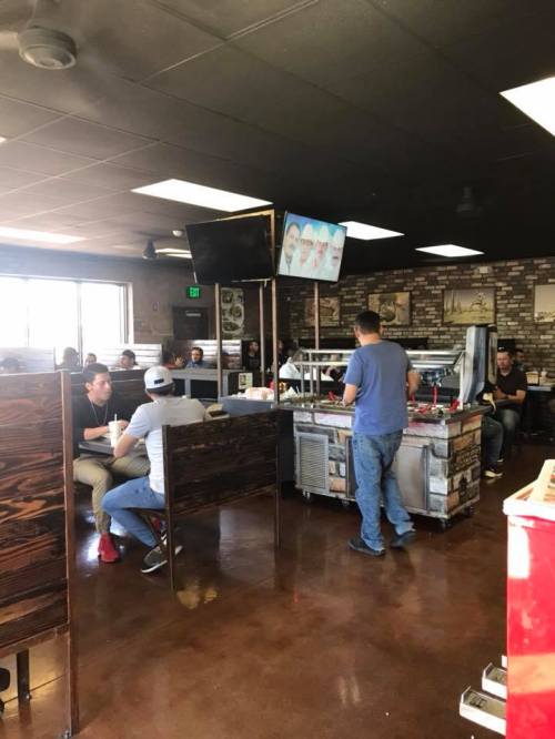 A busy restaurant interior with customers seated at booths and a server attending to a counter. TVs are mounted on the wall.