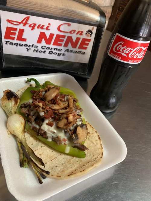 A plate featuring a stuffed green pepper with meat, mushrooms, and cheese, alongside grilled onion and a Coca-Cola bottle.