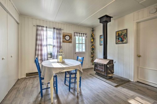 Cozy dining area with a round table, blue chairs, a wood stove, and large windows with checkered curtains.
