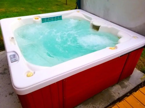A white hot tub with bubbling water, set on a patio with green grass in the background.
