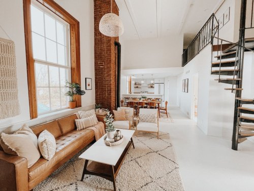 Bright, modern living space with a brown leather sofa, white walls, and a spiral staircase leading to an open dining area.