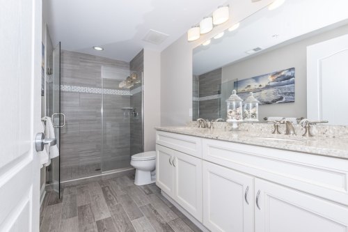 Modern bathroom featuring a glass shower, double vanity with granite countertop, and stylish lighting.
