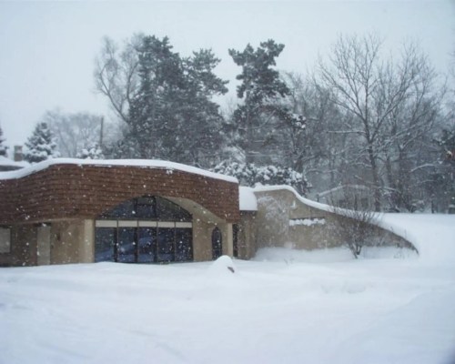 A snow-covered building surrounded by trees, with heavy snowfall creating a wintery scene.
