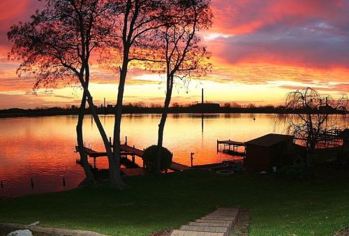 A serene lake at sunset, with vibrant orange and purple skies, silhouetted trees, and a wooden dock.