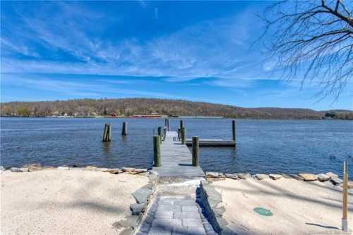 A serene view of a dock extending into a calm river, surrounded by trees and a clear blue sky.