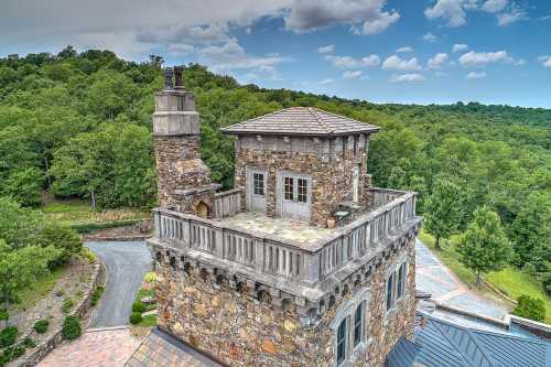 Aerial view of a stone tower surrounded by lush greenery and a winding driveway under a partly cloudy sky.