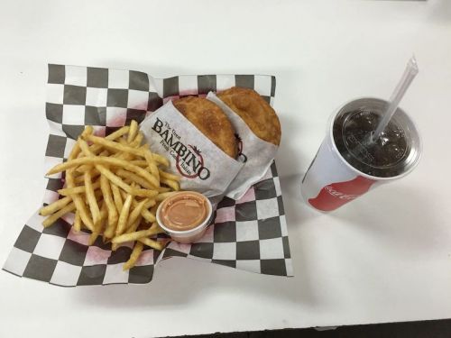 A basket of fries, two sandwiches wrapped in paper, and a cup of soda on a checkered tray.