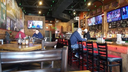 A cozy bar interior with wooden decor, patrons seated at the bar, and multiple TVs showing sports.