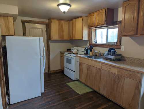 A cozy kitchen featuring wooden cabinets, a white refrigerator, stove, and a sink with dishes drying.