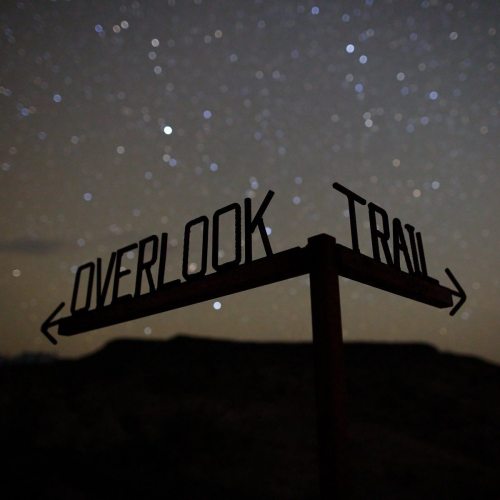 A signpost for "Overlook Trail" silhouetted against a starry night sky.
