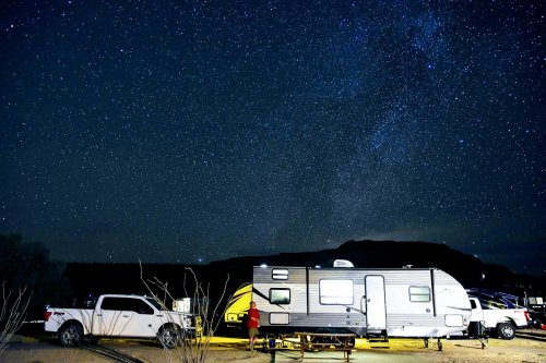 A camper and truck under a starry night sky, with mountains in the background.