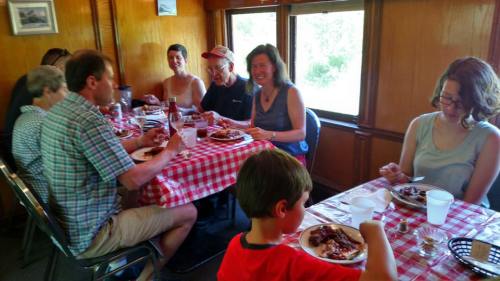 A group of people enjoying a meal together at a table with checkered tablecloths, smiling and sharing food.