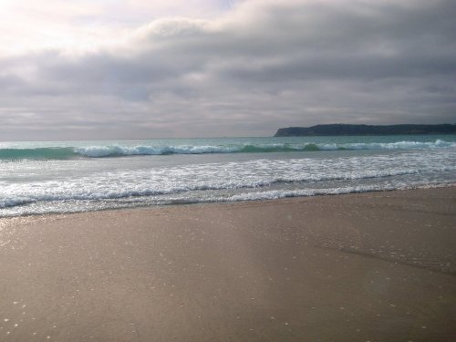A serene beach scene with gentle waves lapping at the shore under a cloudy sky.