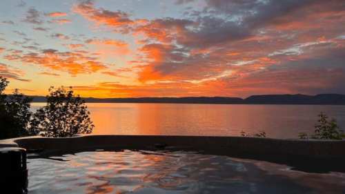 A serene sunset over a calm lake, with vibrant orange and pink clouds reflecting on the water's surface.