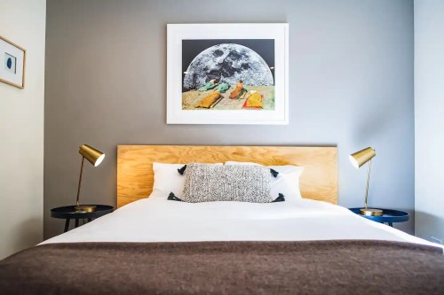 A modern bedroom featuring a wooden bed, decorative pillows, and a moon-themed artwork on the wall.