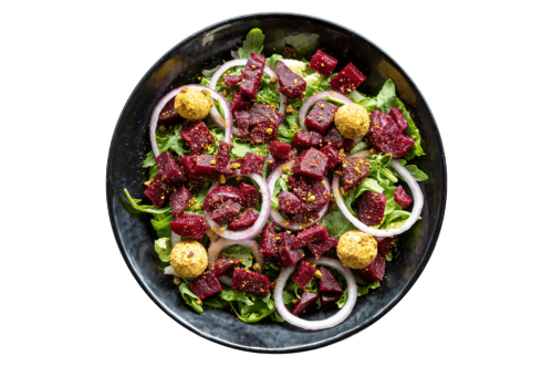 A vibrant salad with beets, greens, onion slices, and round cheese balls, sprinkled with spices in a black bowl.