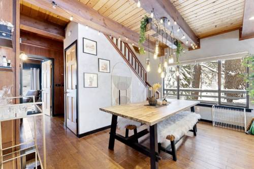 Cozy dining area with a wooden table, string lights, and large windows overlooking a snowy landscape.