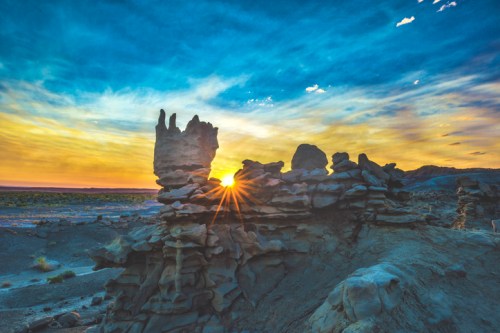 A stunning sunset behind unique rock formations, casting a warm glow over a desert landscape.