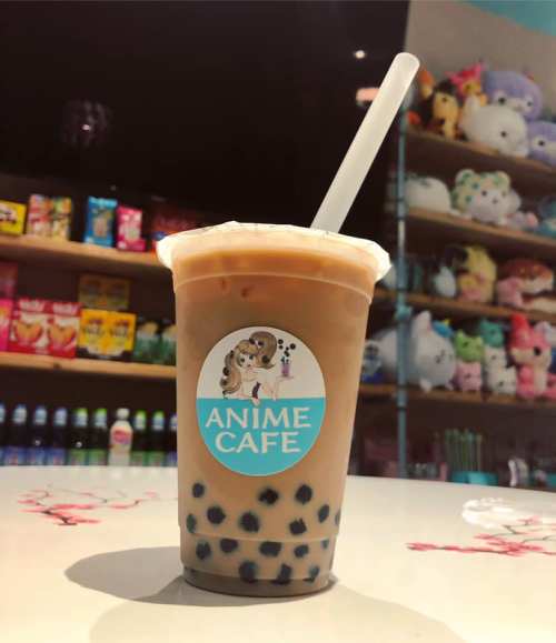 A cup of bubble tea with a logo reading "Anime Cafe," set against a colorful background of snacks and plush toys.