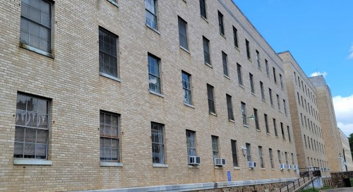A brick building with multiple windows, some with air conditioning units, under a clear blue sky.