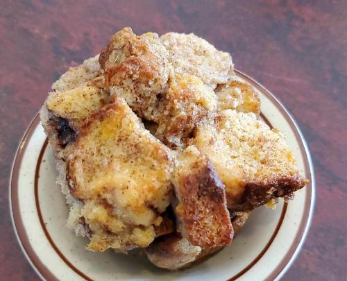 A close-up of a baked dessert on a small plate, featuring a golden-brown, crumbly texture with a dusting of cinnamon.