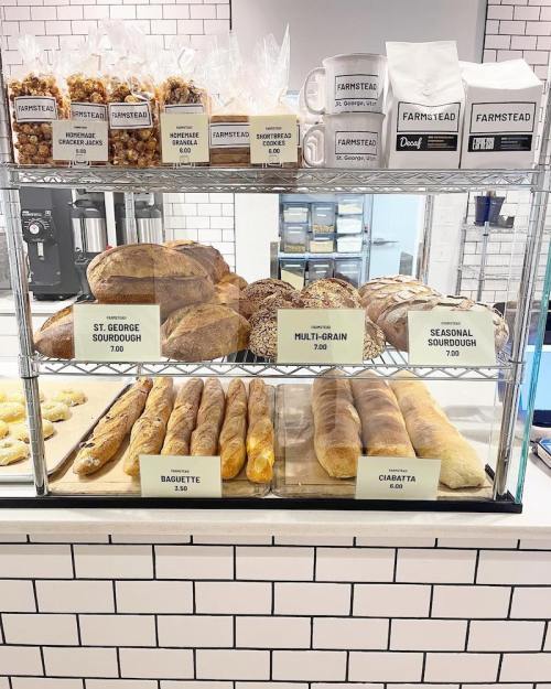 A display case filled with various breads, including sourdough, baguettes, and ciabatta, with prices labeled.