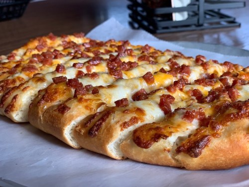 A freshly baked pizza topped with melted cheese and crispy bacon, served on a white paper.