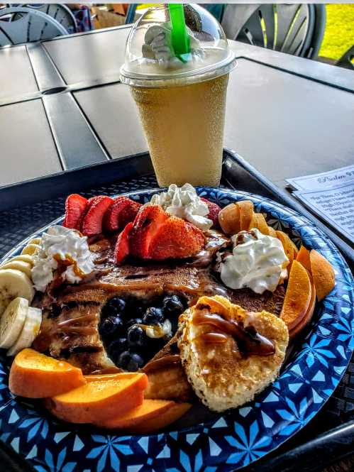 A colorful breakfast plate with pancakes topped with fruit, whipped cream, and a milkshake in a cup.