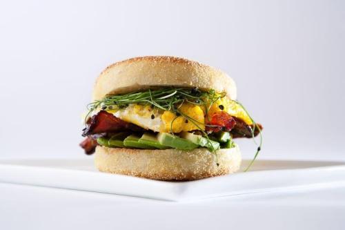 A delicious sandwich with layers of egg, bacon, corn, and greens, served on a toasted English muffin.
