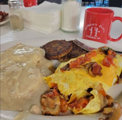 A plate of omelet filled with vegetables, served with gravy and biscuits, alongside hash browns and a red coffee mug.
