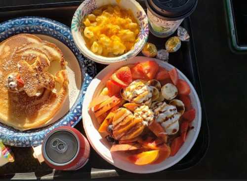 A tray with pancakes, fruit salad, macaroni and cheese, a drink, and candy.