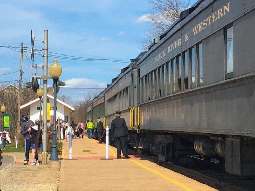 A vintage train at a station with passengers boarding and waiting, set against a clear blue sky.