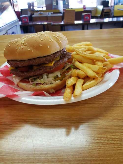 A large hamburger with lettuce, tomato, and cheese, served with a side of golden French fries on a paper plate.