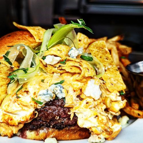 A close-up of a gourmet burger topped with cheese, crispy tortilla strips, and green onions, served with fries.