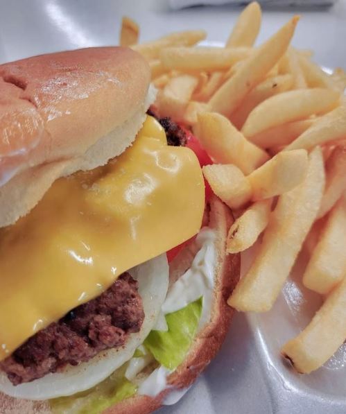 A cheeseburger with lettuce, tomato, and onion, served with a side of golden French fries on a plate.