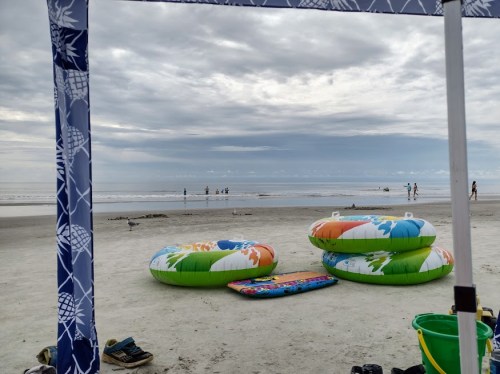Colorful inflatable rings on a sandy beach, with people in the distance and a cloudy sky overhead.